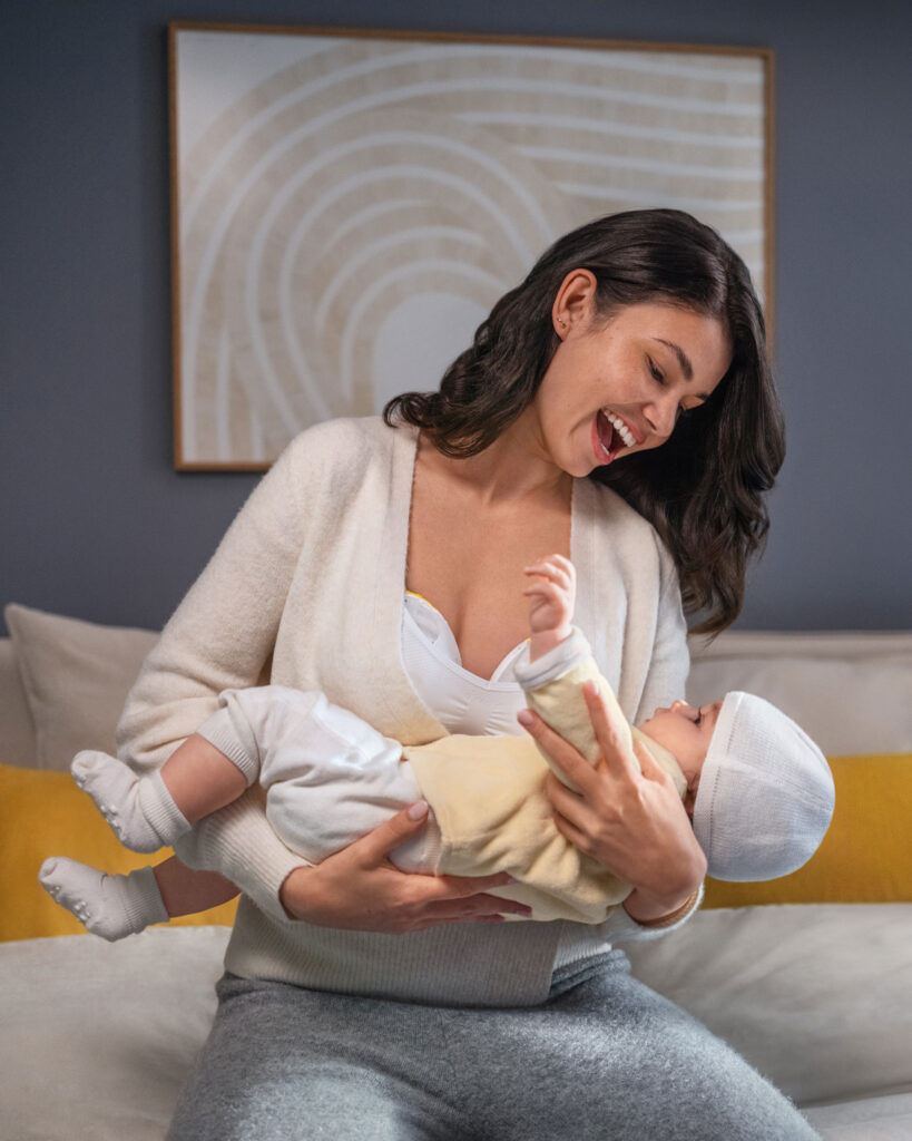 Mum cradling baby while using Medela Magic inbra pump
